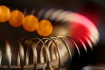 A coil spring arcs through the picture; there are 4 transparent orange dots coming in from the upper left and a red transparent blob on the right side of the image.