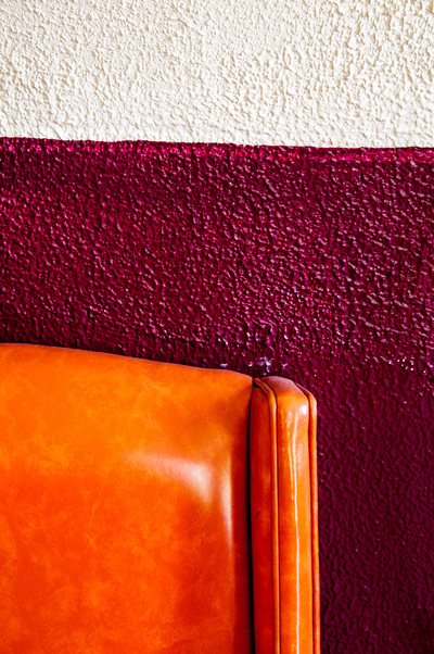 A nubbly wall painted white at the top of the image and maroon in the lower three quarters. A smooth orange chair back is visible in the lower left corner.