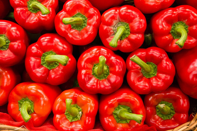 A stack of red sweet peppers with their green stems facing the camera fills the frame.