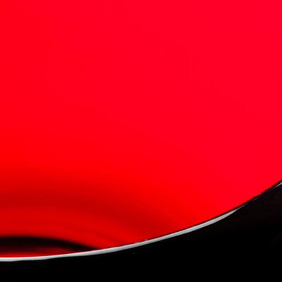 A square image of clear red, there is an arc of black from lower left corner to halfway up on the right edge.