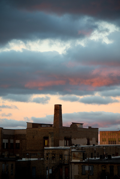 A brick smokestack with sunset colored clouds over it