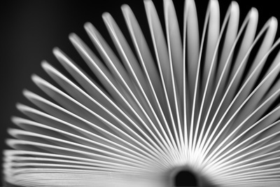 Gray-and-white side view of an arched slinky in front of a dark background