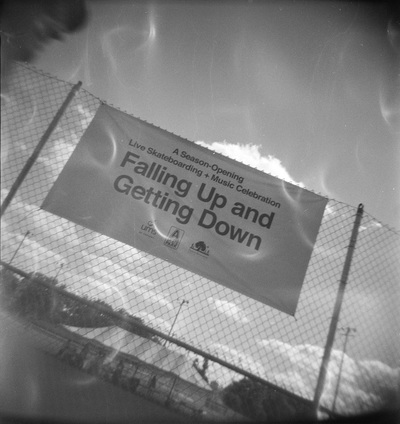 Sign on a chainlink fence, photographed at an angle, reads 'Falling Up and Getting Down'